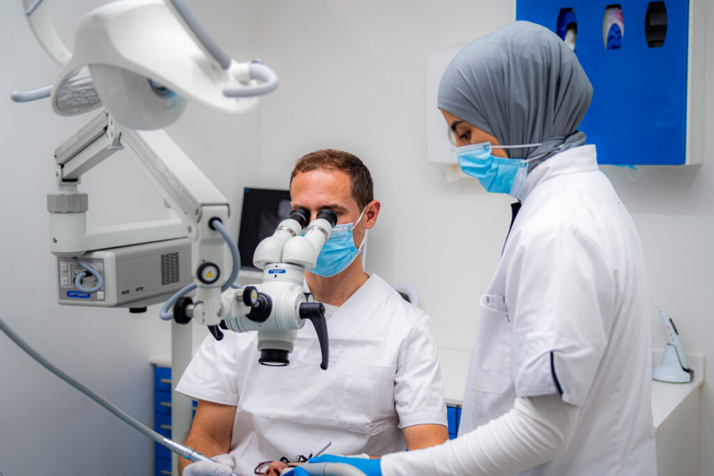 Dentista che lavora con un microscopio operatorio insieme a un'assistente presso 3D Tandarts